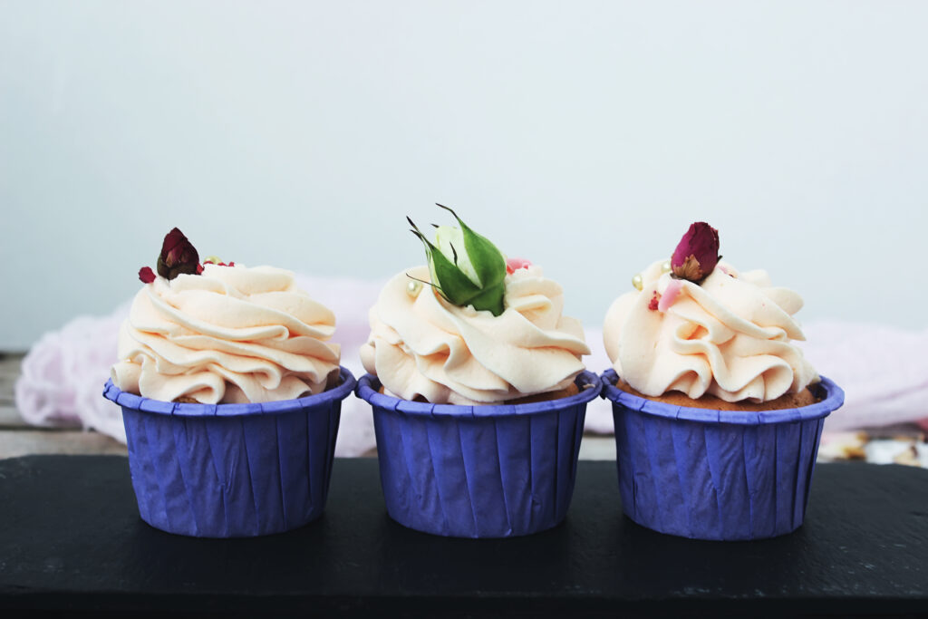 Food Grade Paper Muffin Cups Built for High Volume Professional Baking tasty cupcakes with delicate cream in a lilac stand, decorated with flowers on a white table
